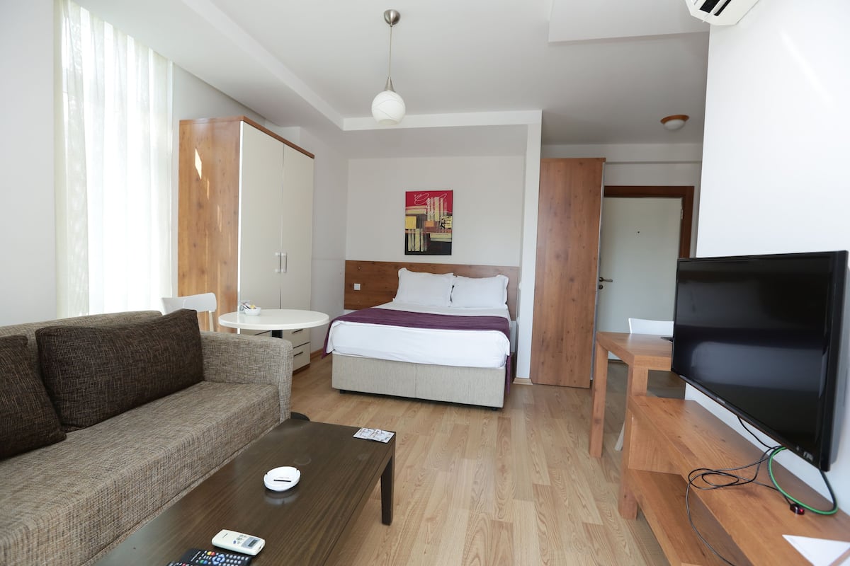 A hotel room with a bed, a sofa, a TV, a coffee table, and a small table with a lamp.