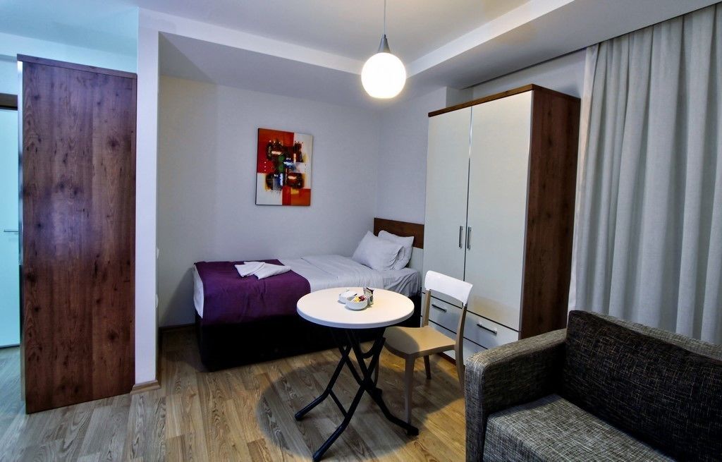 Quarto de hotel compacto com cama, mesinha, cadeira, guarda-roupa e um quadro na parede.