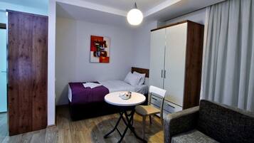 Quarto de hotel compacto com cama, mesinha, cadeira, guarda-roupa e um quadro na parede.