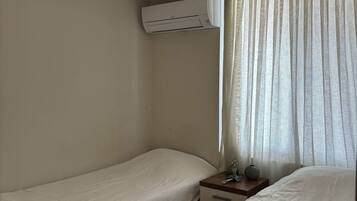 Ein Zimmer mit zwei Einzelbetten, einem Nachttisch mit einer Vase und einer kleinen Skulptur sowie einer Wand-Klimaanlage.
