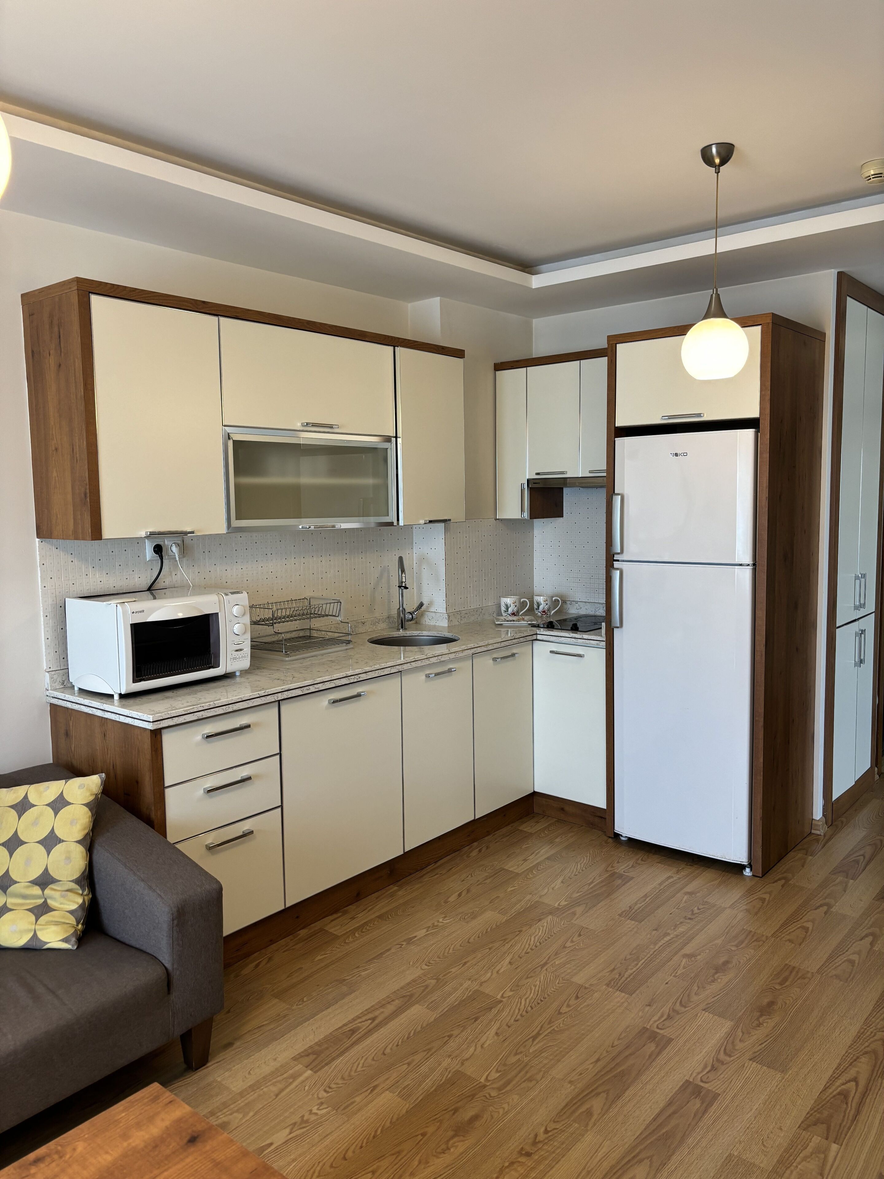 Una cocina compacta con armarios blancos, un microondas, un fregadero y un refrigerador.