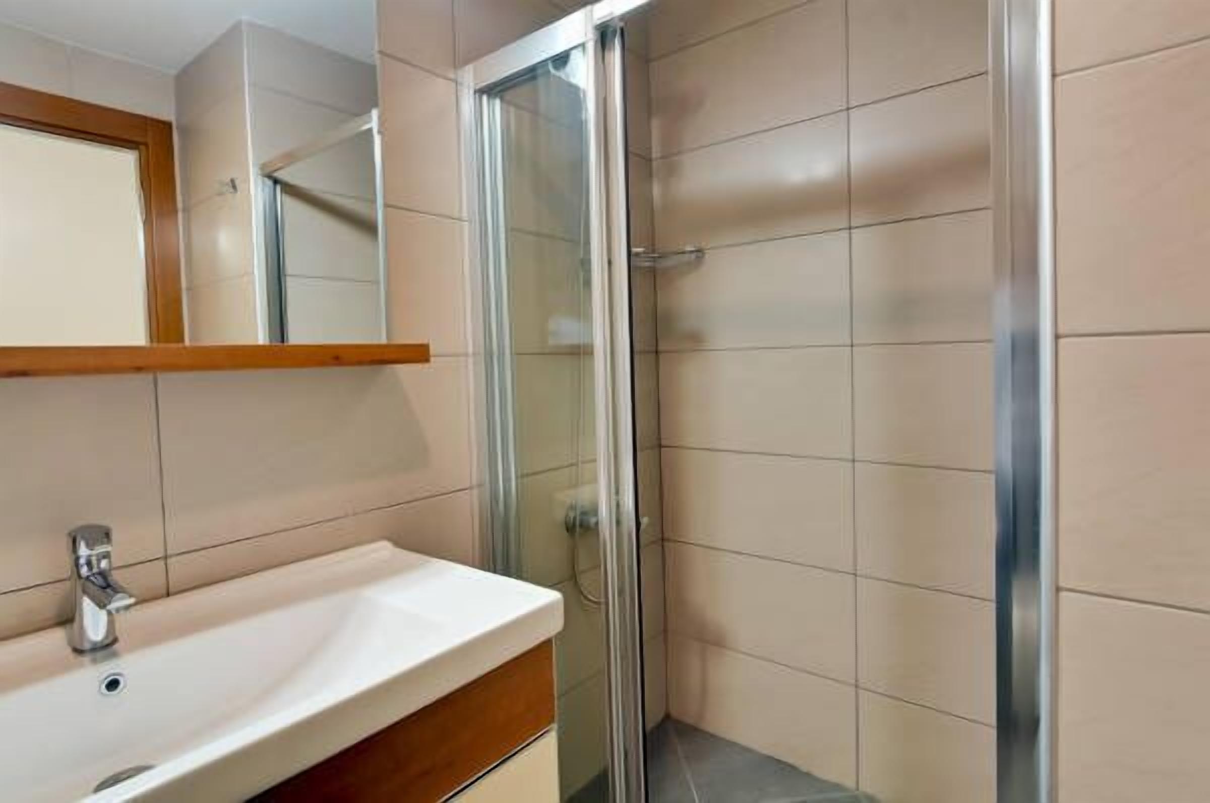 Un baño con lavamanos blanco, espejo y cabina de ducha de vidrio.