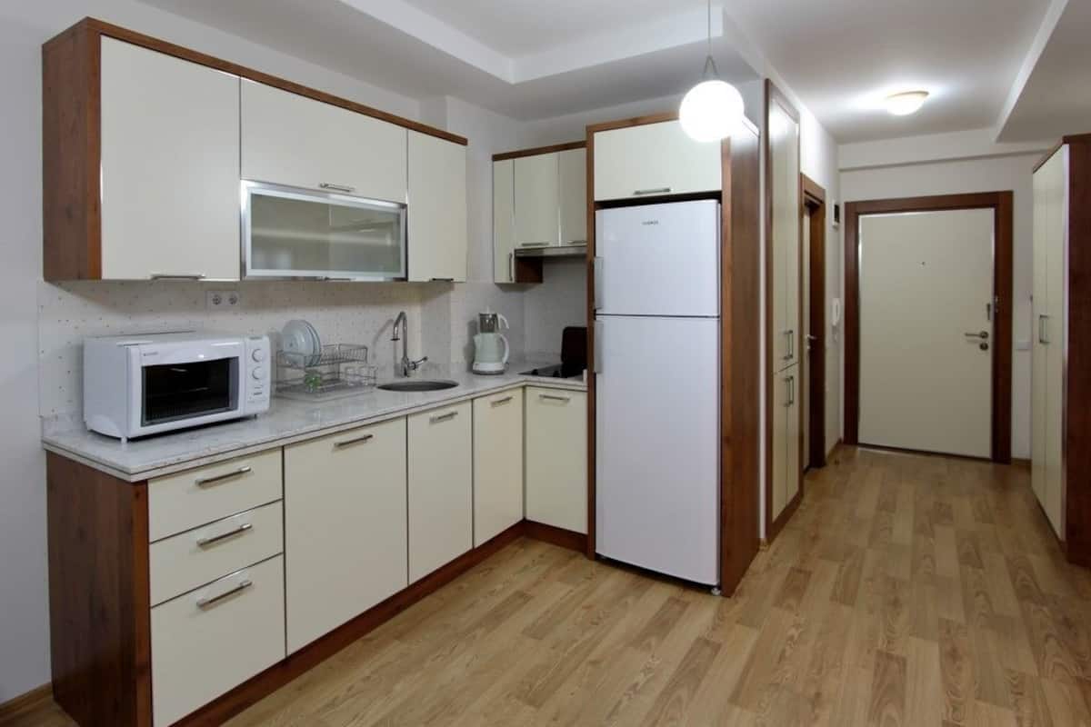 A compact kitchen with white cabinets, a microwave, a refrigerator, and a sink.