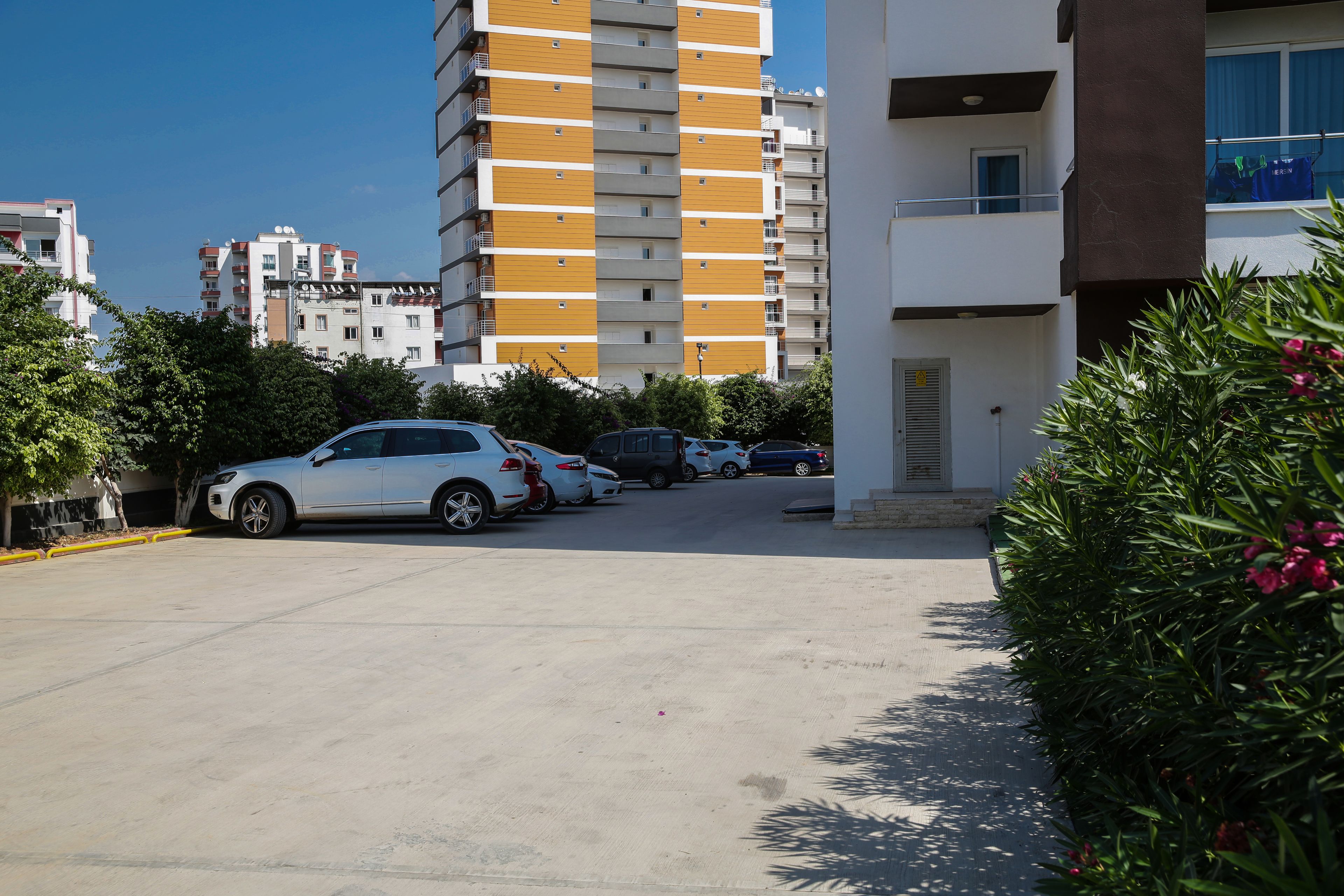 Un parking avec plusieurs voitures, un immeuble doté de balcons et quelques espaces verts.