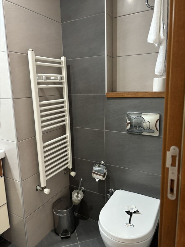 A modern bathroom with a white toilet, a towel rack, a trash bin, and a toilet paper holder. - Upart Home (Mersin)