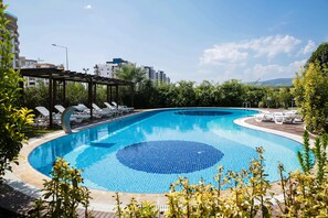 A swimming pool with lounge chairs and a pergola, surrounded by greenery and buildings in the background. - Upart Home (Mersin)