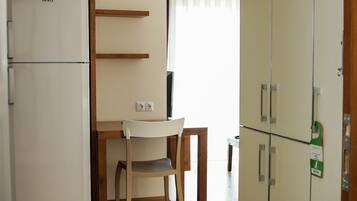 Une pièce de taille modeste comprenant un coin cuisine, une chaise en bois, une petite table et une armoire.