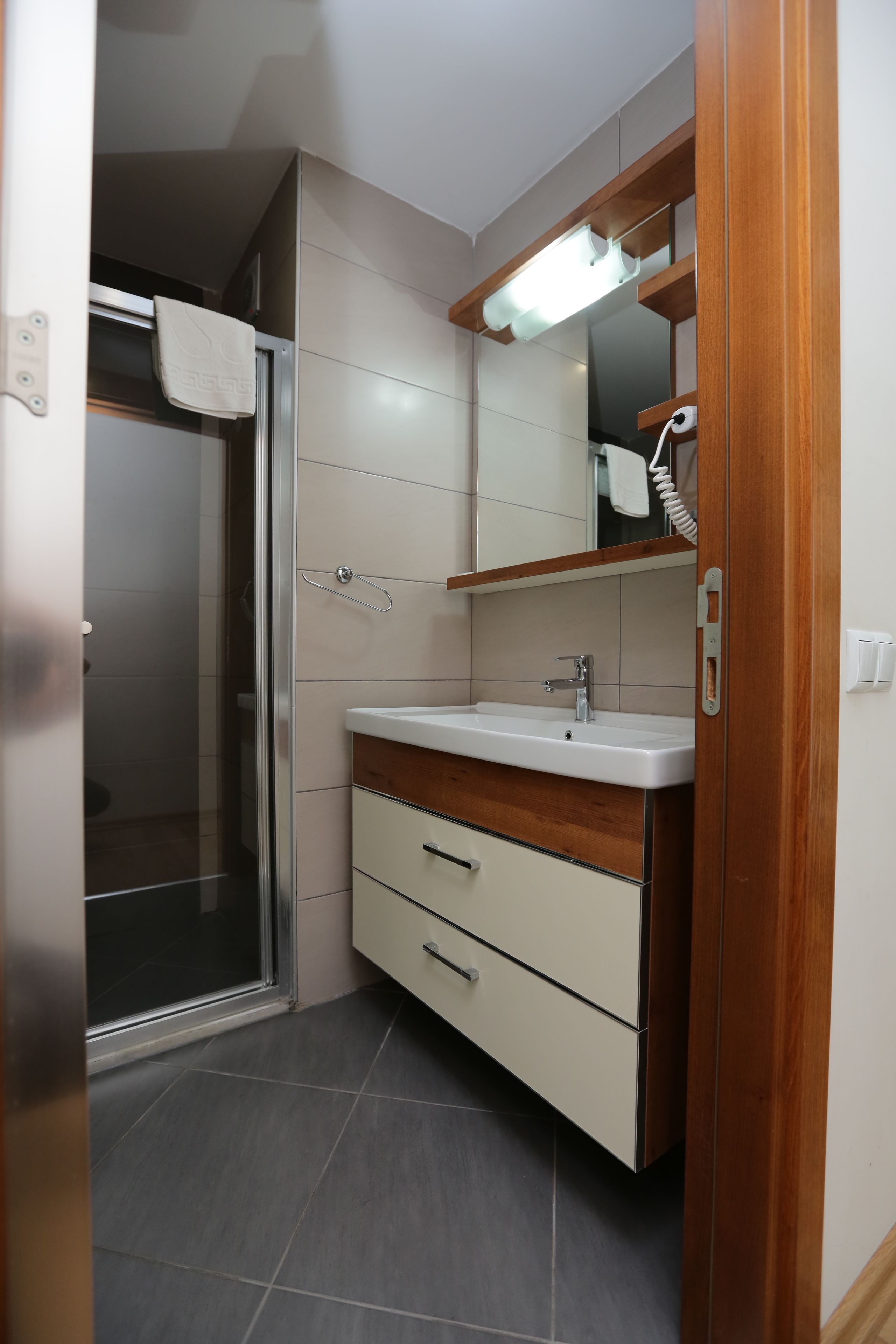A modern bathroom with a glass shower enclosure, a wooden vanity with a sink, and a mirror above.