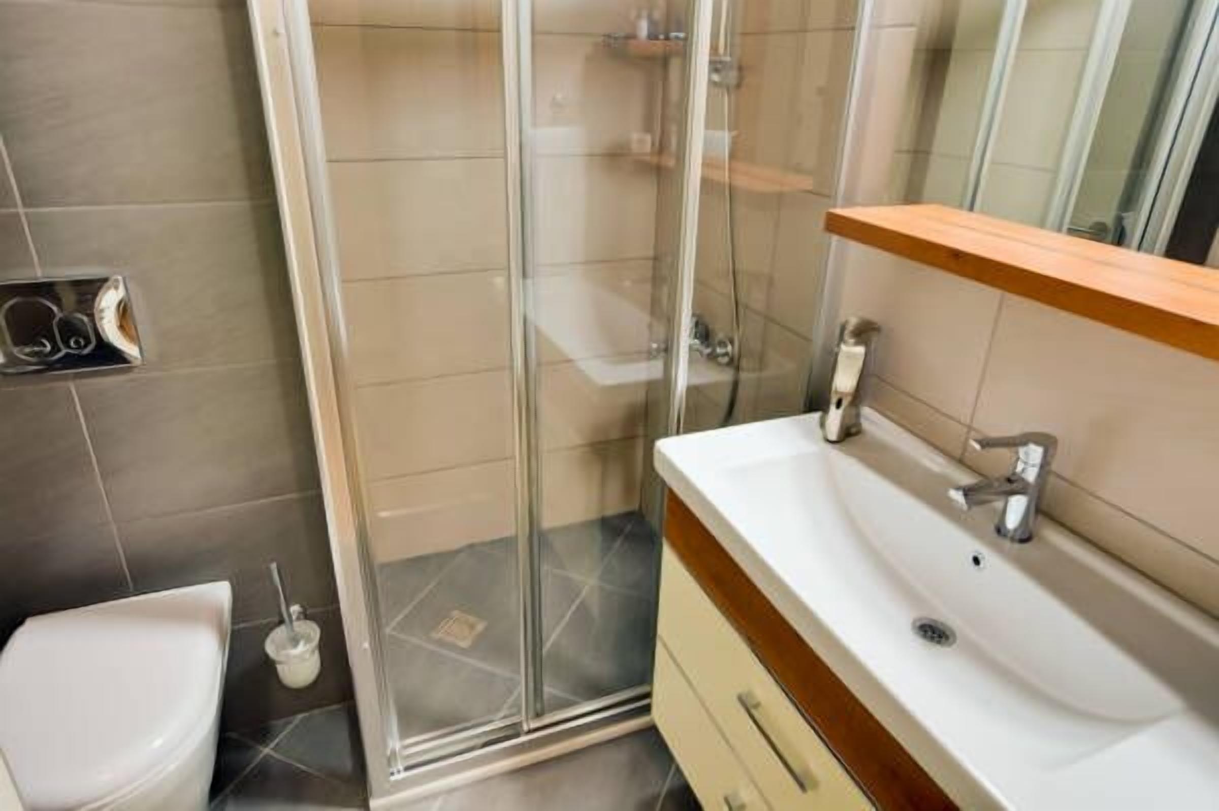 Un baño con cabina de ducha de vidrio, un lavabo blanco y un mueble de tocador de madera.