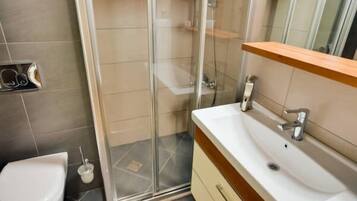 Un baño con cabina de ducha de vidrio, un lavabo blanco y un mueble de tocador de madera.