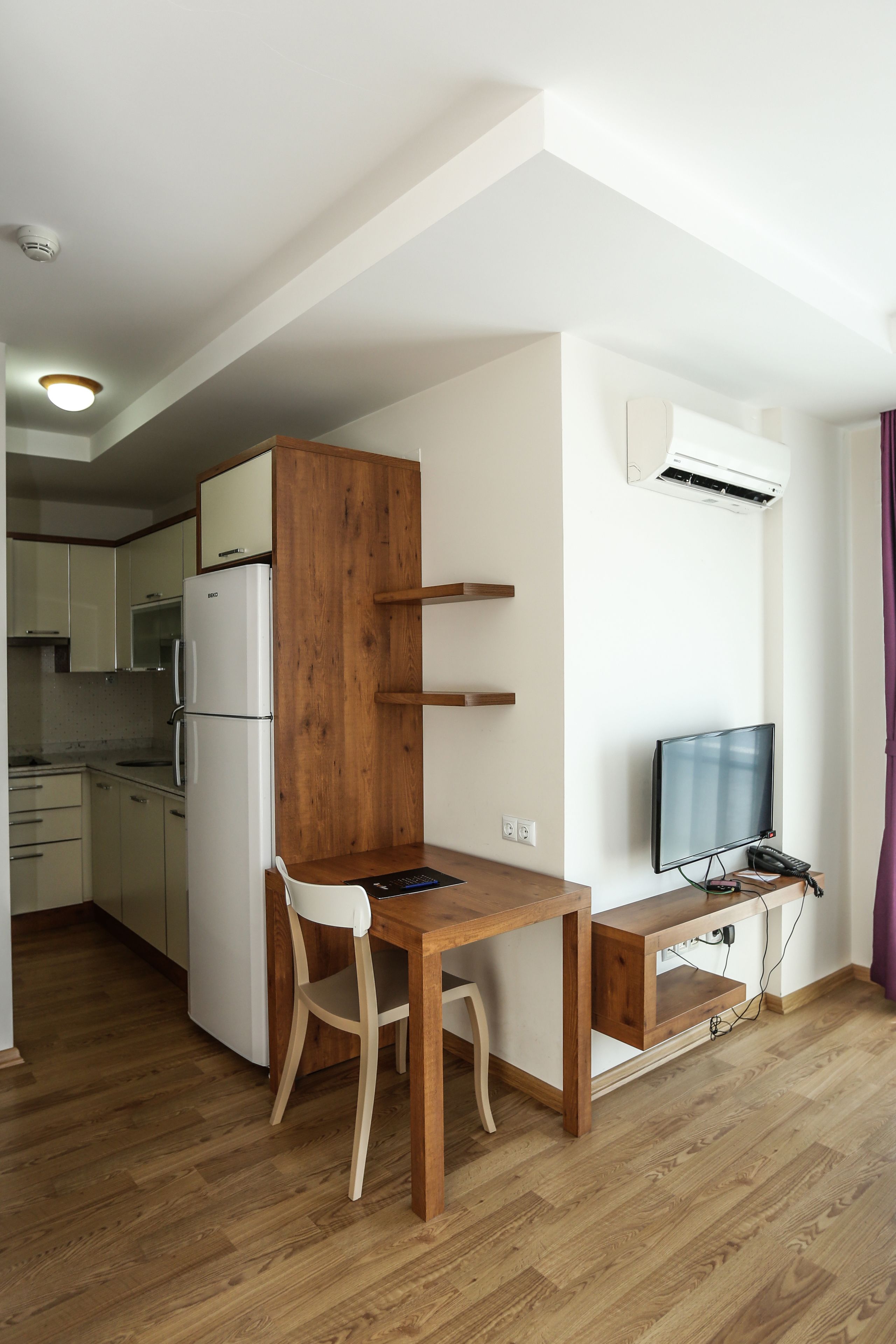 Eine kleine Küche mit Kühlschrank, Holzschrank und Essbereich mit Tisch und Stuhl.
