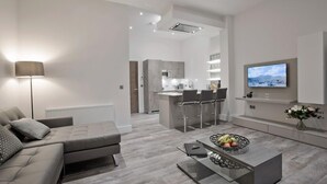 Un salon moderne avec un canapé, une table basse et un téléviseur. Il y a également un coin cuisine avec un bar et des sièges.