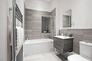 A modern bathroom with a bathtub, vanity, and toilet. - Apple Apartments Devanha Gardens (Aberdeen)