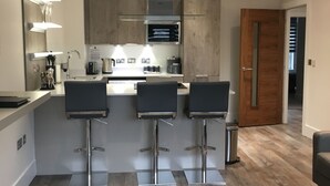 Une cuisine moderne avec un îlot central, des tabourets de bar et une porte en bois.