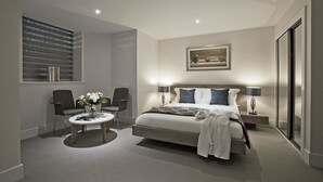 Une chambre à coucher moderne avec un grand lit, deux fauteuils, une table basse ronde et un tableau au mur.