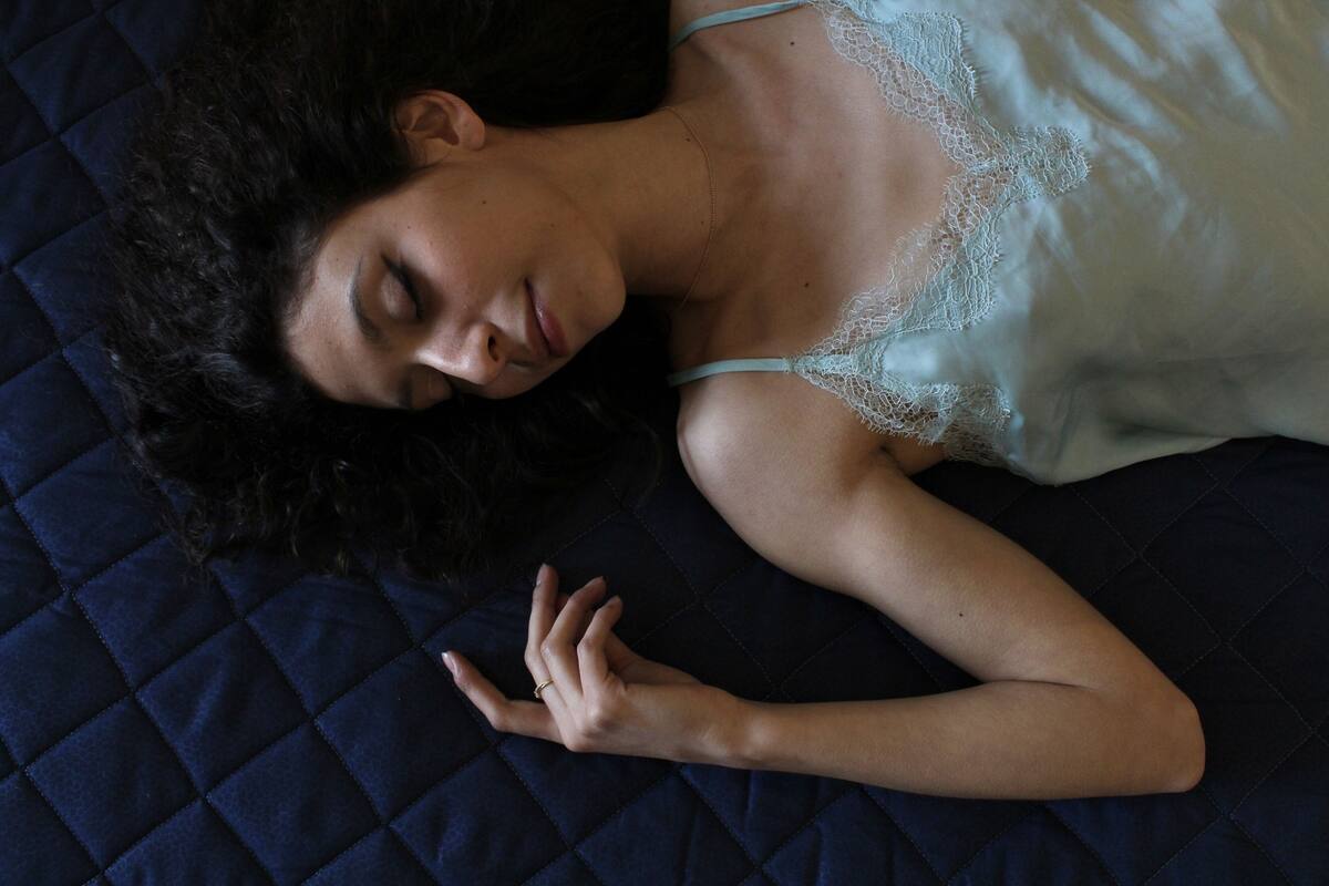 A person lying on a dark quilted bed with lace details on the bedding.