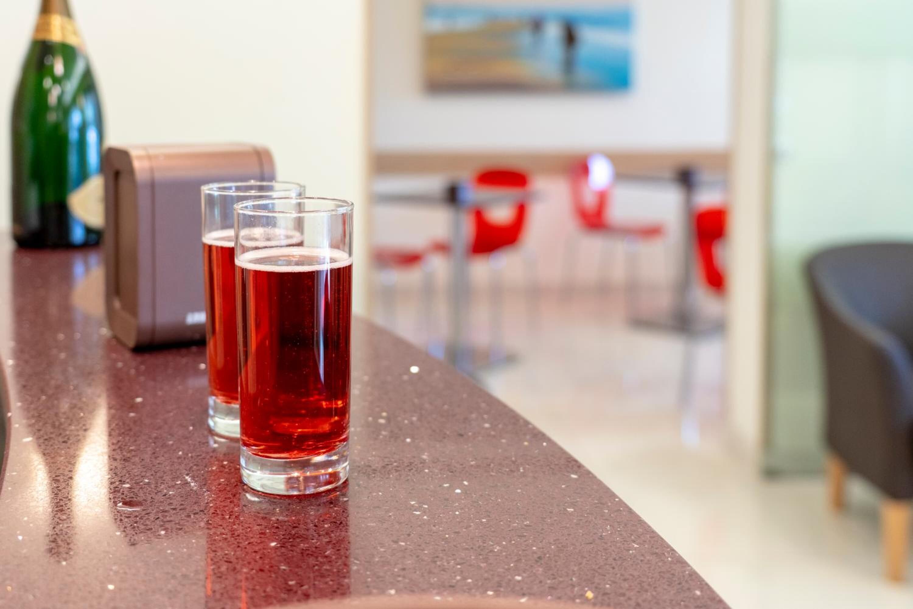 A bar area with glasses of red beverage, a bottle, and a cash register.