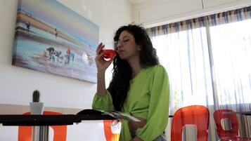 A woman sitting at a table with a painting of a beach scene, a cactus, and red chairs.