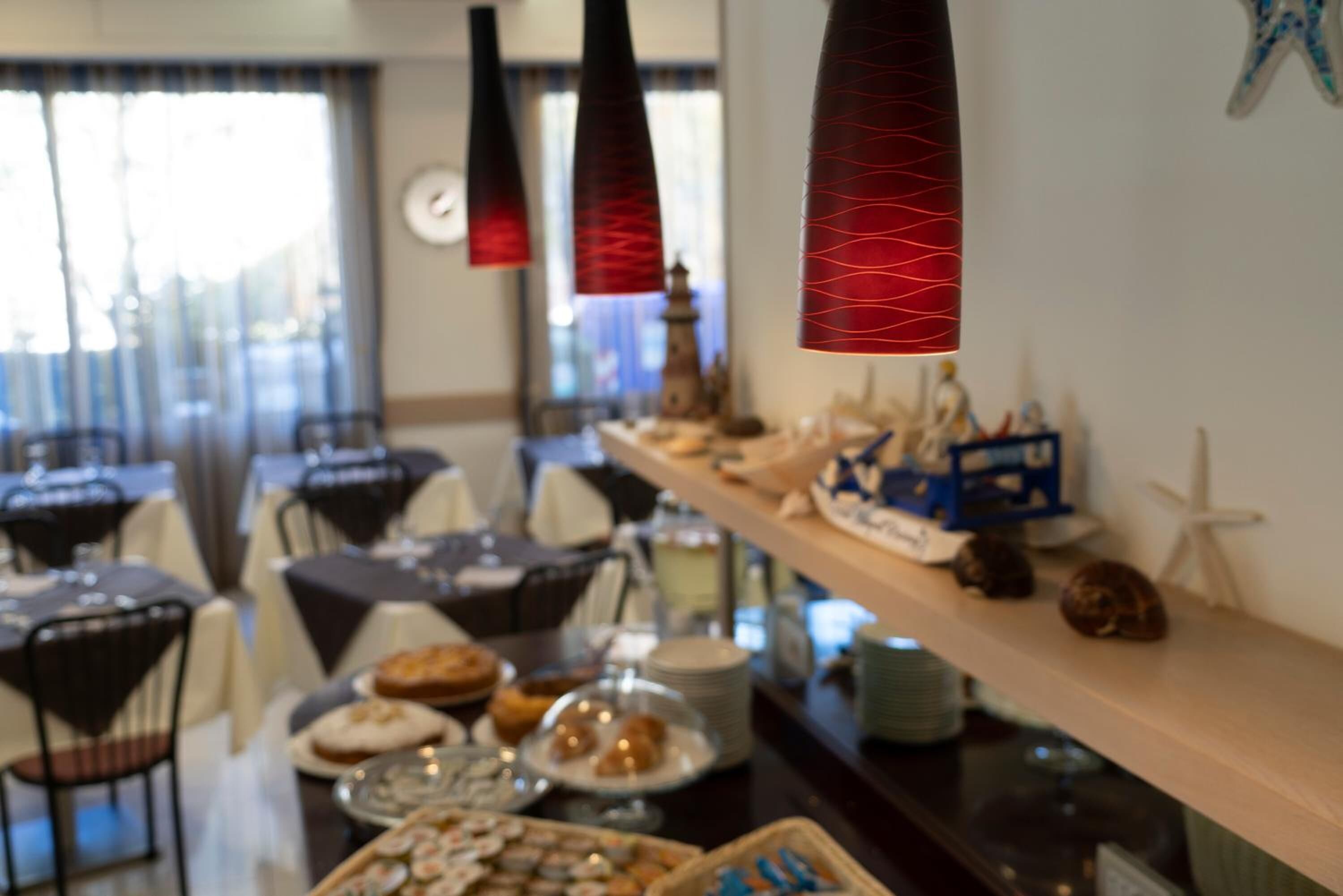 Un comedor con mesas dispuestas para el desayuno, un bufé con diversas opciones de comida y elementos decorativos como un modelo de barco y estrellas de mar.