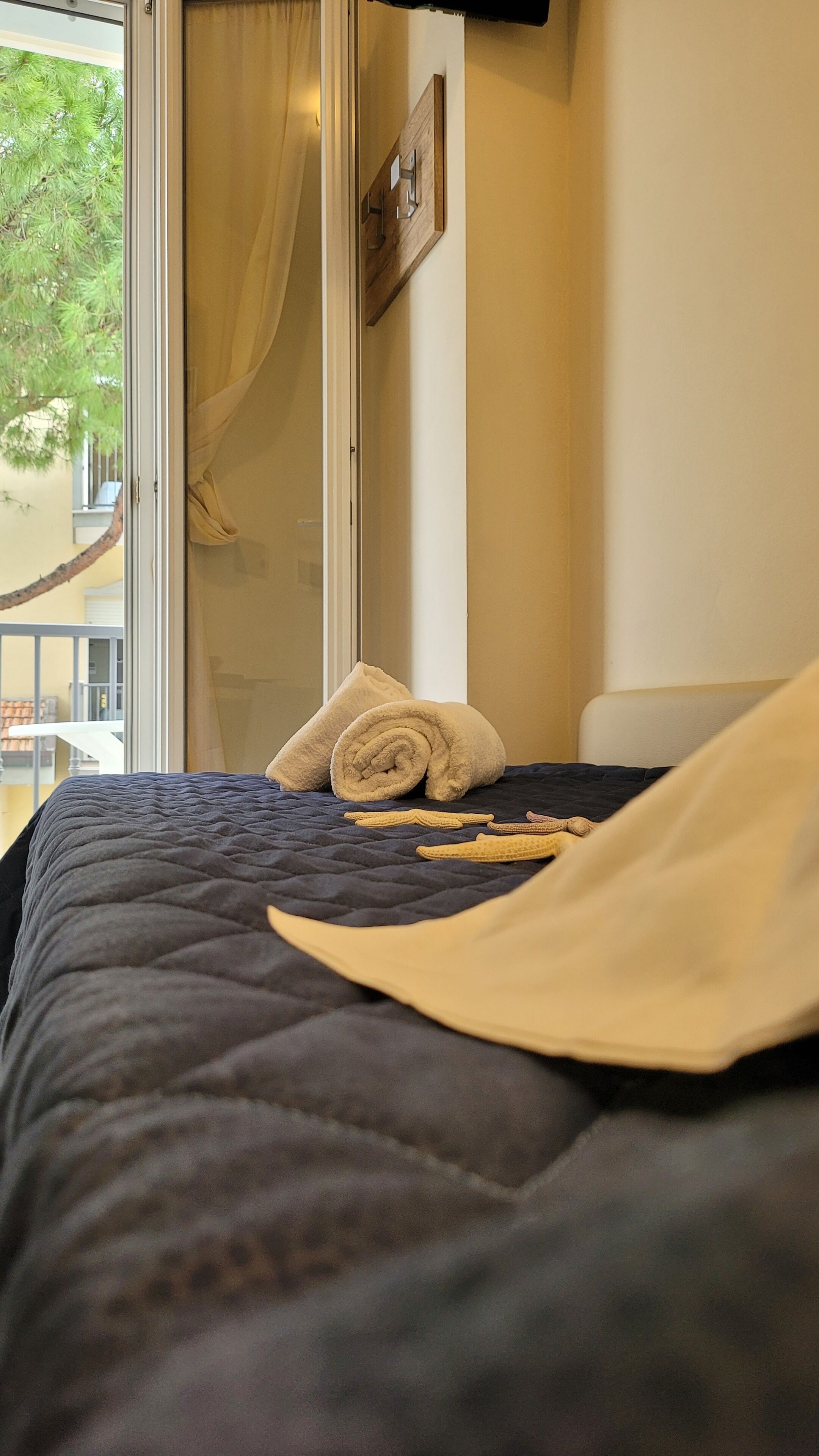 Ein Hotelzimmer mit Bett, einem Vorhangfenster, einem Holz-Kopfteil und Blick auf Bäume.
