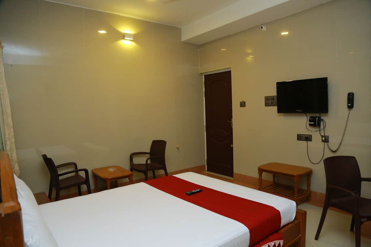A hotel room with a bed, two chairs, a small table, a television, and a door.