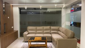 Un salon moderne avec un canapé d’angle beige, une table basse en bois et une cloison en verre.