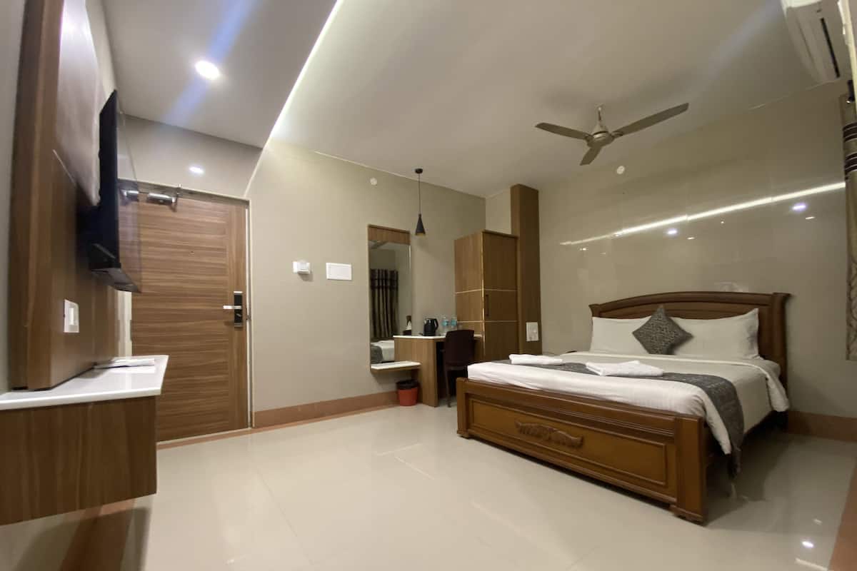 A modern bedroom with a wooden bed, a ceiling fan, a TV mounted on the wall, and a desk with a chair.
