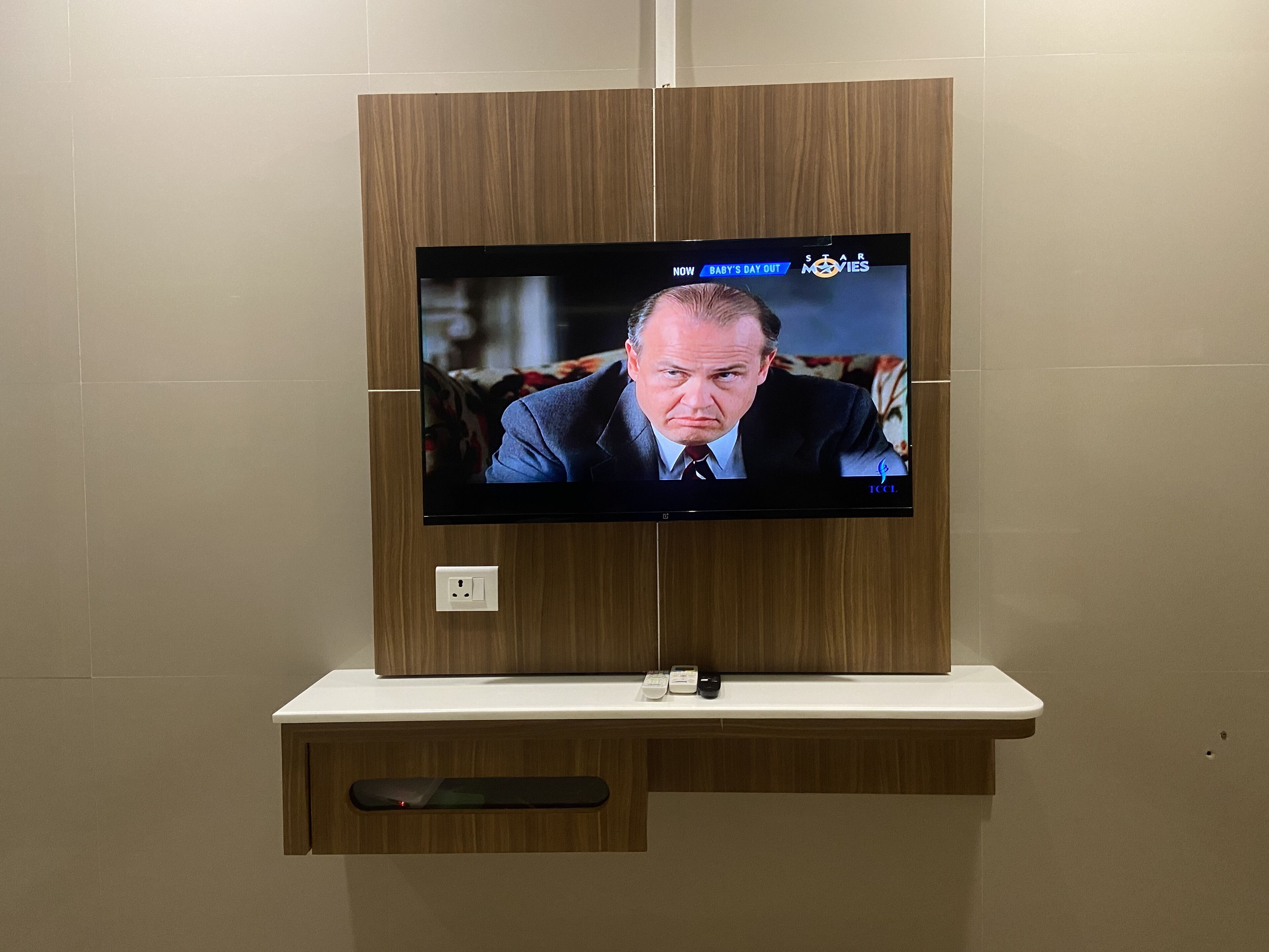 Un televisore fissato a una parete di legno, con un telecomando e una presa di corrente sotto.