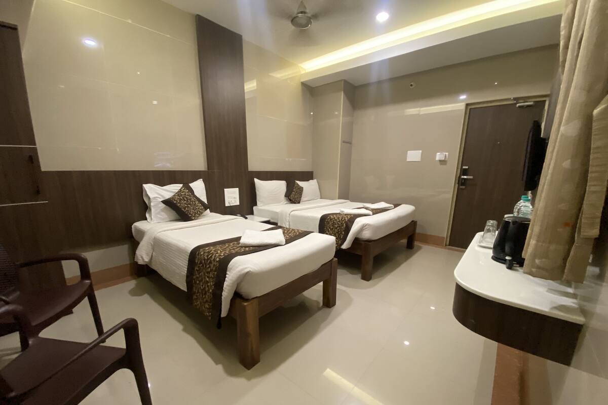 A hotel room with two beds, a wooden chair, a small table with a kettle, and a door.