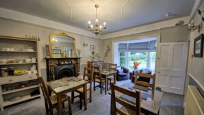 A dining area with a chandelier, wooden chairs, and a table. There is a fireplace with a mirror above it. - West End Guest House (Richmond)