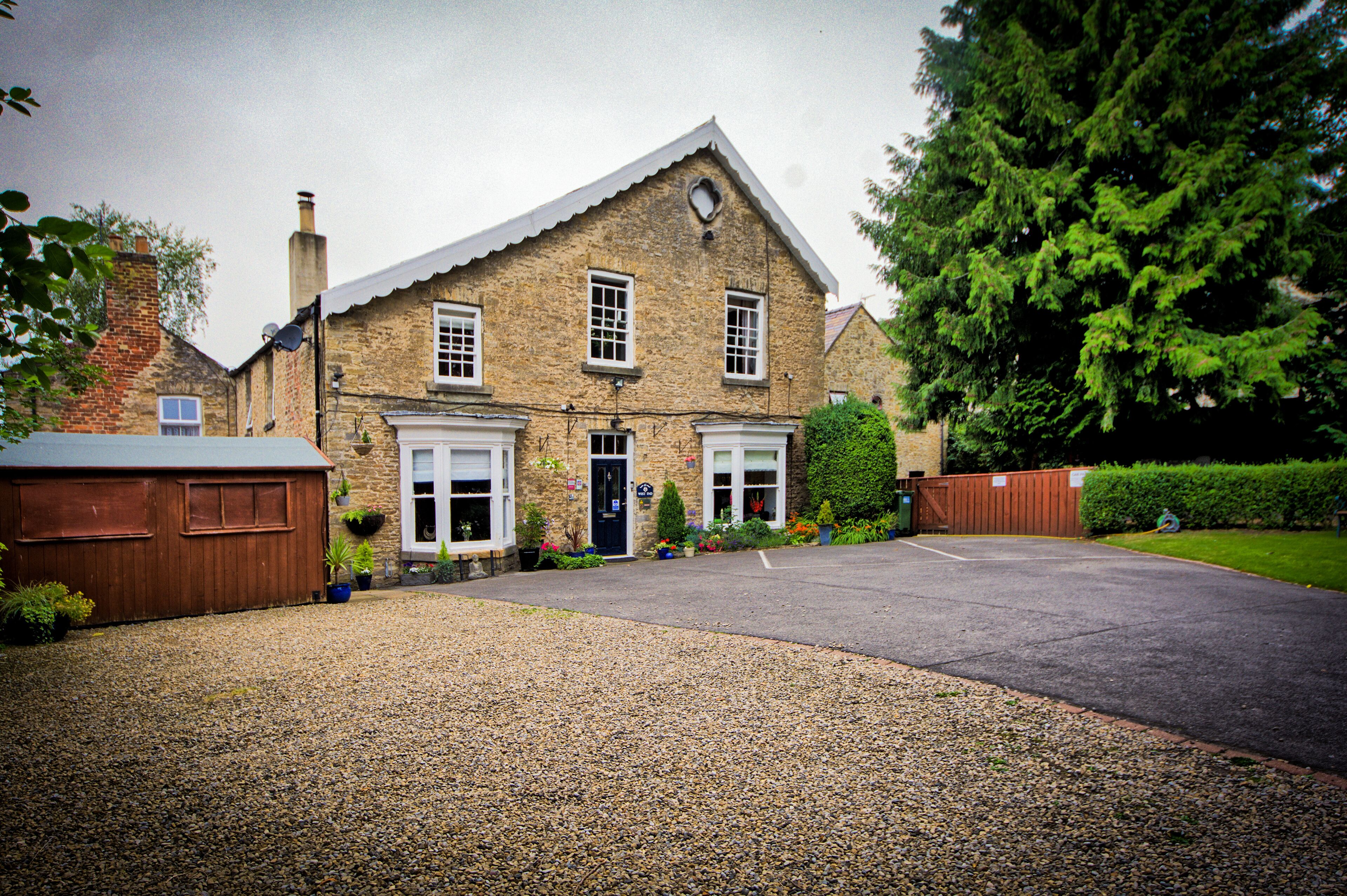 A two-story stone building with a symmetrical facade, a central entrance, and a gravel driveway.