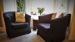 Two dark leather armchairs with cushions, a small wooden table, and a vase with flowers on a carpeted floor. - West End Guest House (Richmond)
