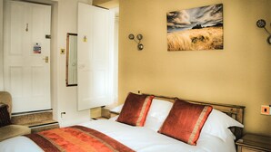 A hotel room with a bed, a nightstand, a chair, and a painting on the wall. - West End Guest House (Richmond)