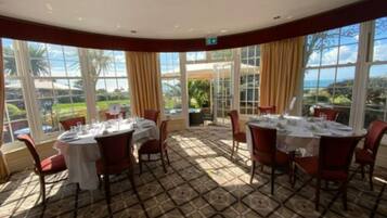 A dining area with round tables and chairs, large windows with curtains, and a patterned floor.