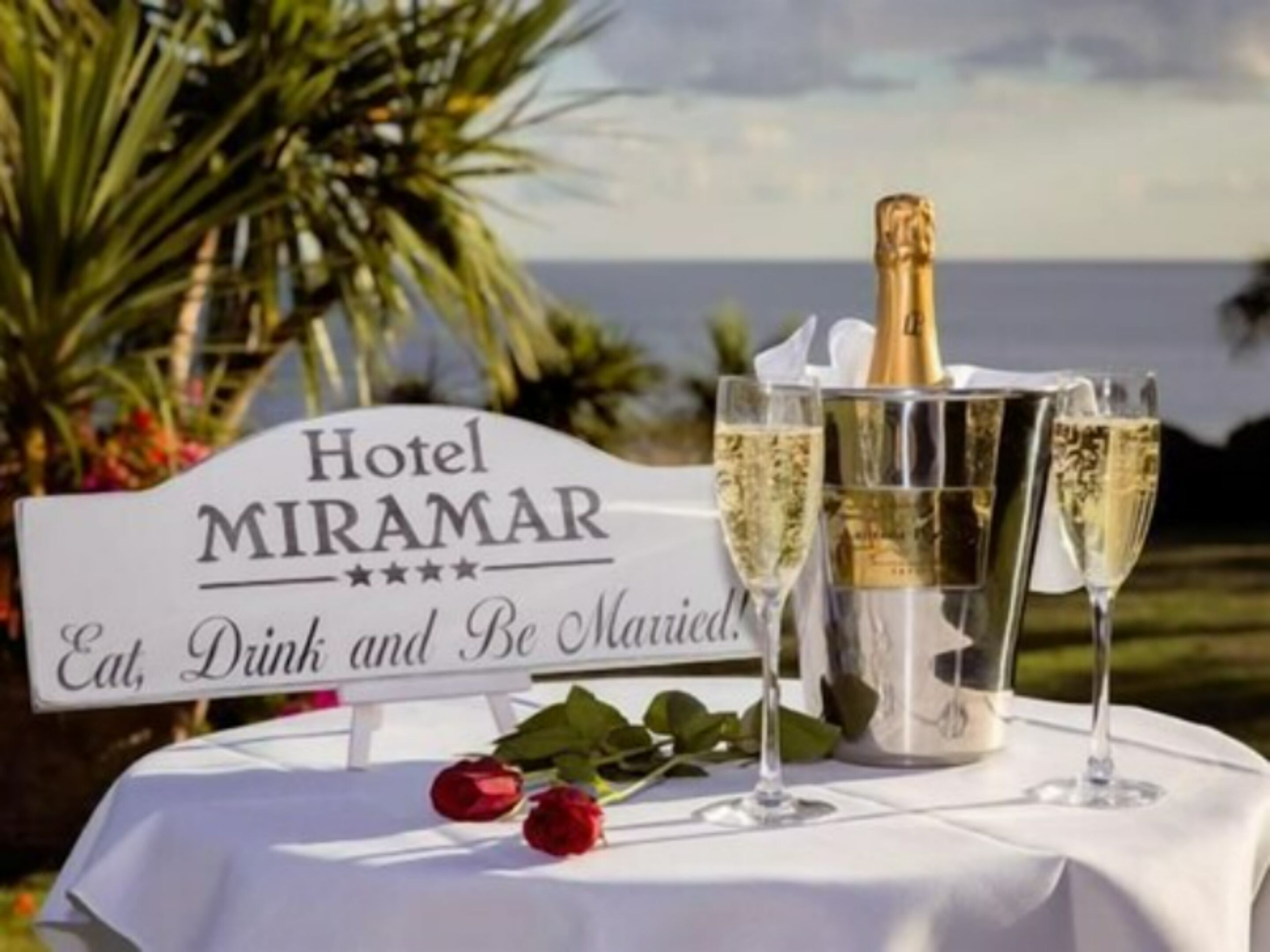 A table with a sign reading "Hotel MIRAMAR Eat, Drink and Be Married!" and a bottle of champagne.