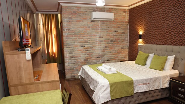 Quarto de hotel com parede de tijolos, cama com roupa de cama verde e branca, mesa de cabeceira, televisão e unidade de ar condicionado.