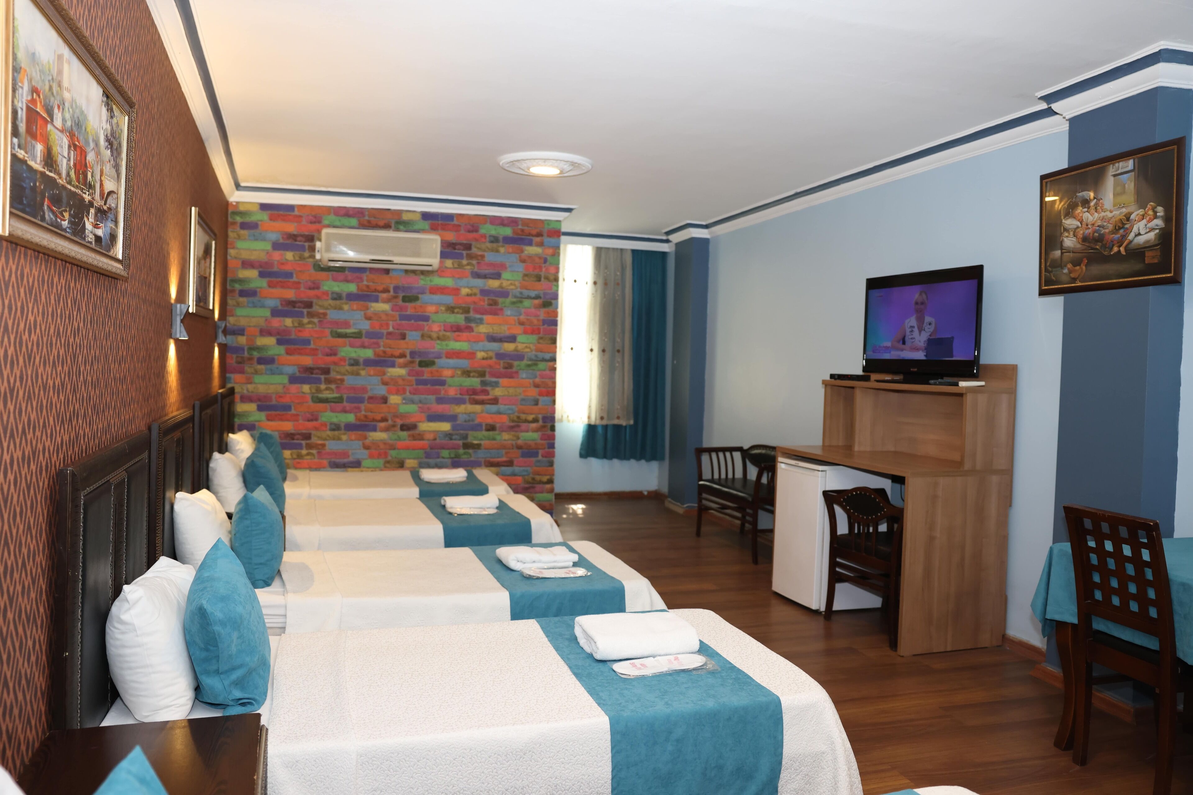 A hotel room with two beds, a desk, a television, and a brick-patterned wall.