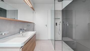 Ein modernes Badezimmer mit einer Duschkabine aus Glas, einem weißen Waschbecken mit Holzschrank und einem großen Spiegel.