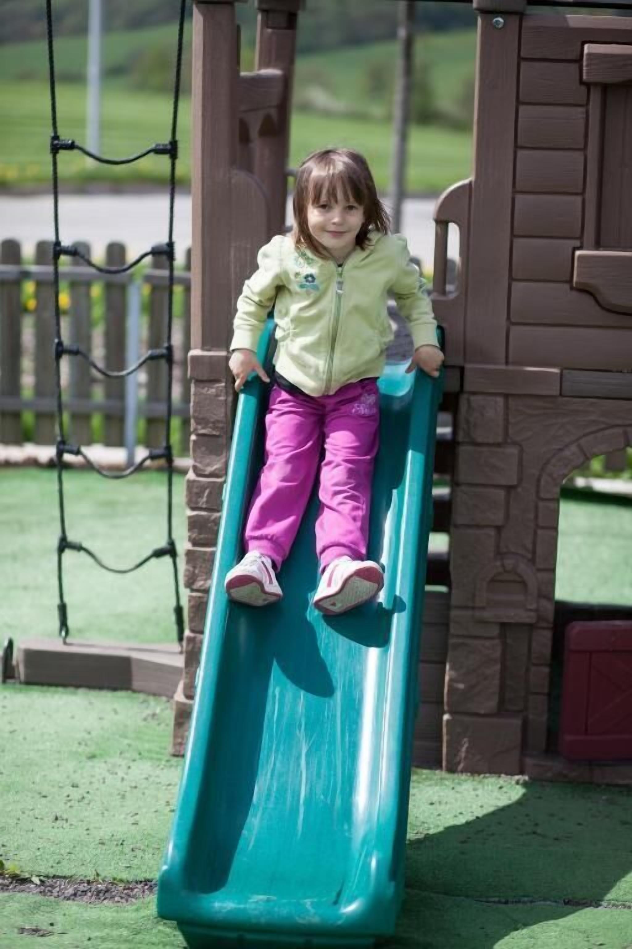 Un niño en un tobogán verde en un parque infantil.