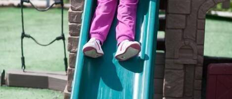 Un niño en un tobogán verde en un parque infantil.