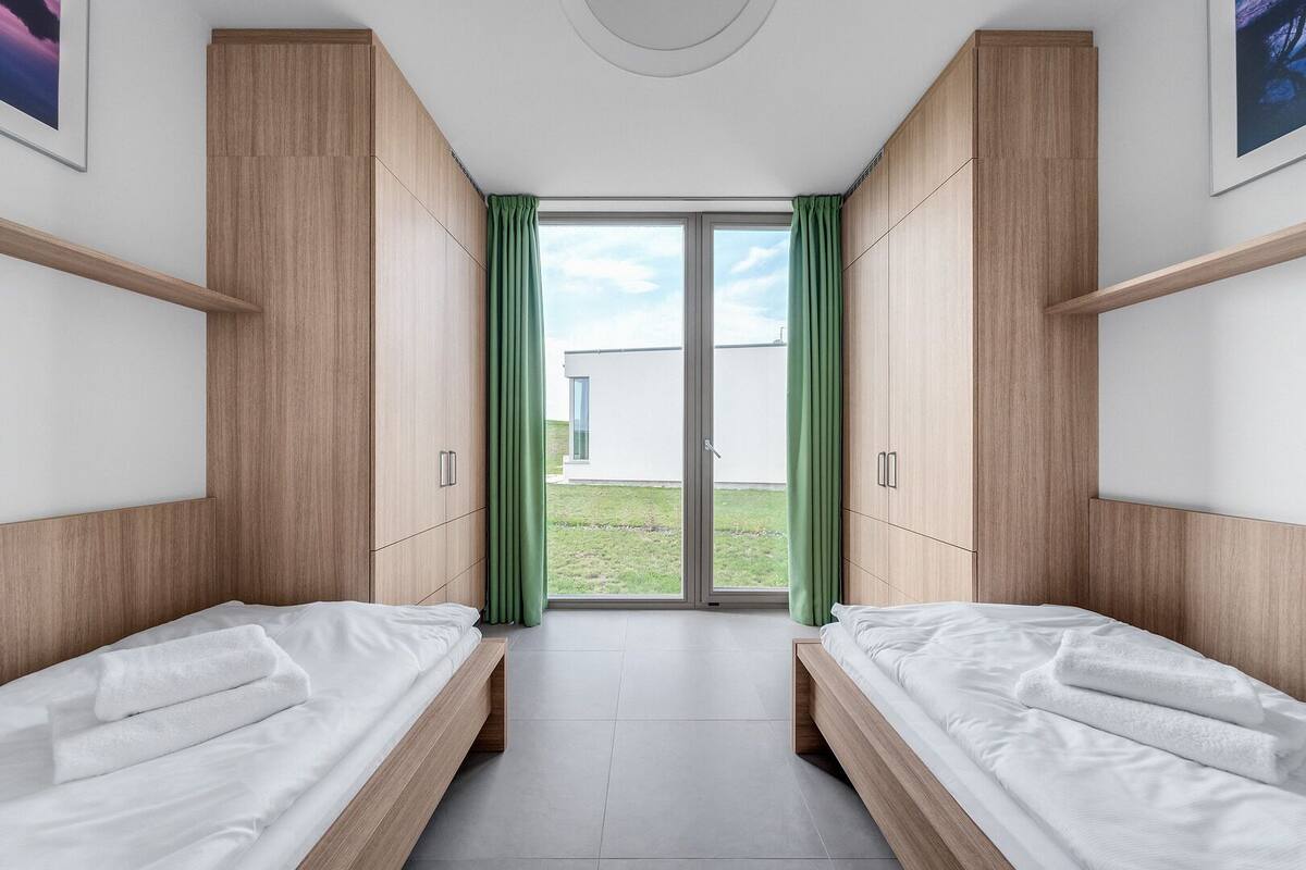 Un dormitorio moderno con dos camas, armarios de madera y una puerta corrediza de vidrio que da a un balcón.