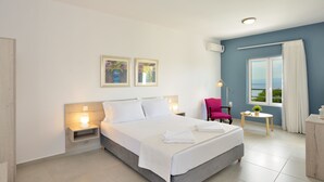 Een moderne hotelkamer met een groot bed, een nachtkastje met lamp, een stoel, een kleintje tafeltje met een plant en een raam met gordijnen.
