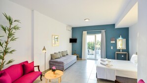 Een moderne kamer met een bank, een bed, een kleintje tafeltje met een bloem, een televisie en een raam met gordijnen.