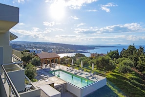 A rooftop pool with lounge chairs and umbrellas, overlooking a scenic landscape with a body of water and hills. - Casa Manolesos (Chania)
