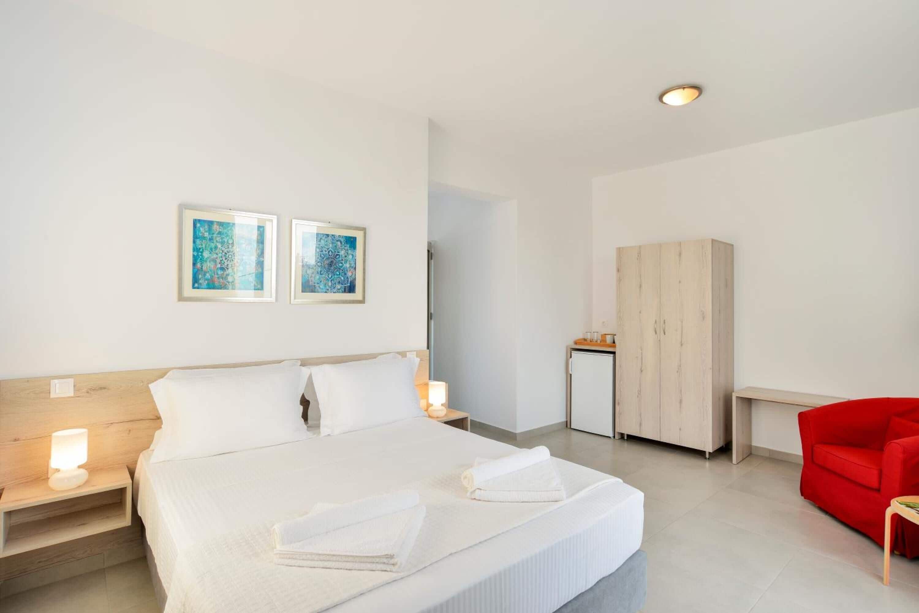 Hotellihuone, jossa on sänky, yöpöydät, vaatekaappi ja taideteoksia seinällä.