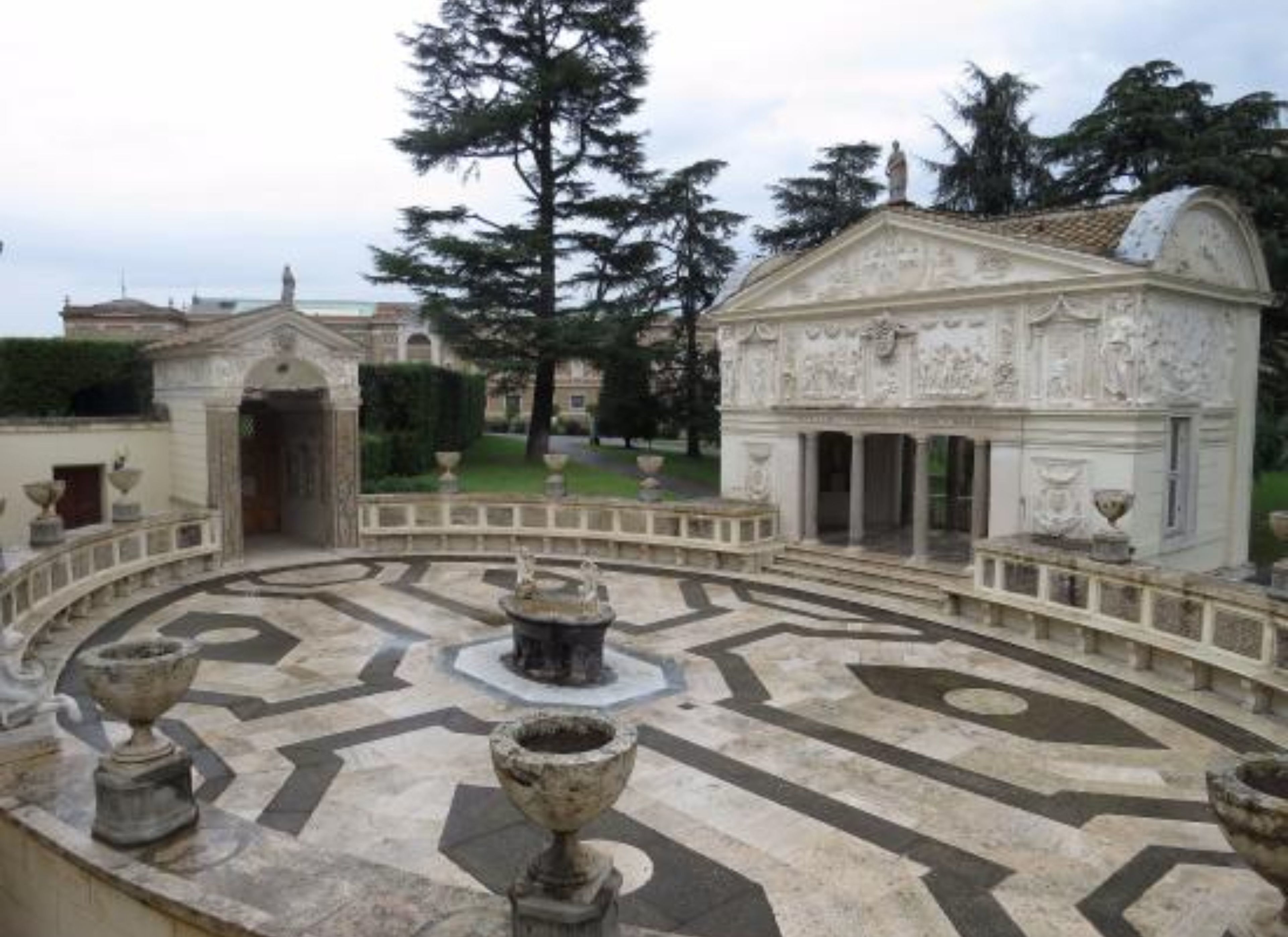 A courtyard with a fountain, a statue, and a building with classical architecture.