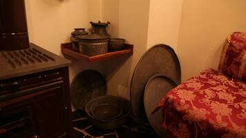A corner of a room with a wooden cabinet, a shelf with pots, a bowl, and a patterned red bedspread.