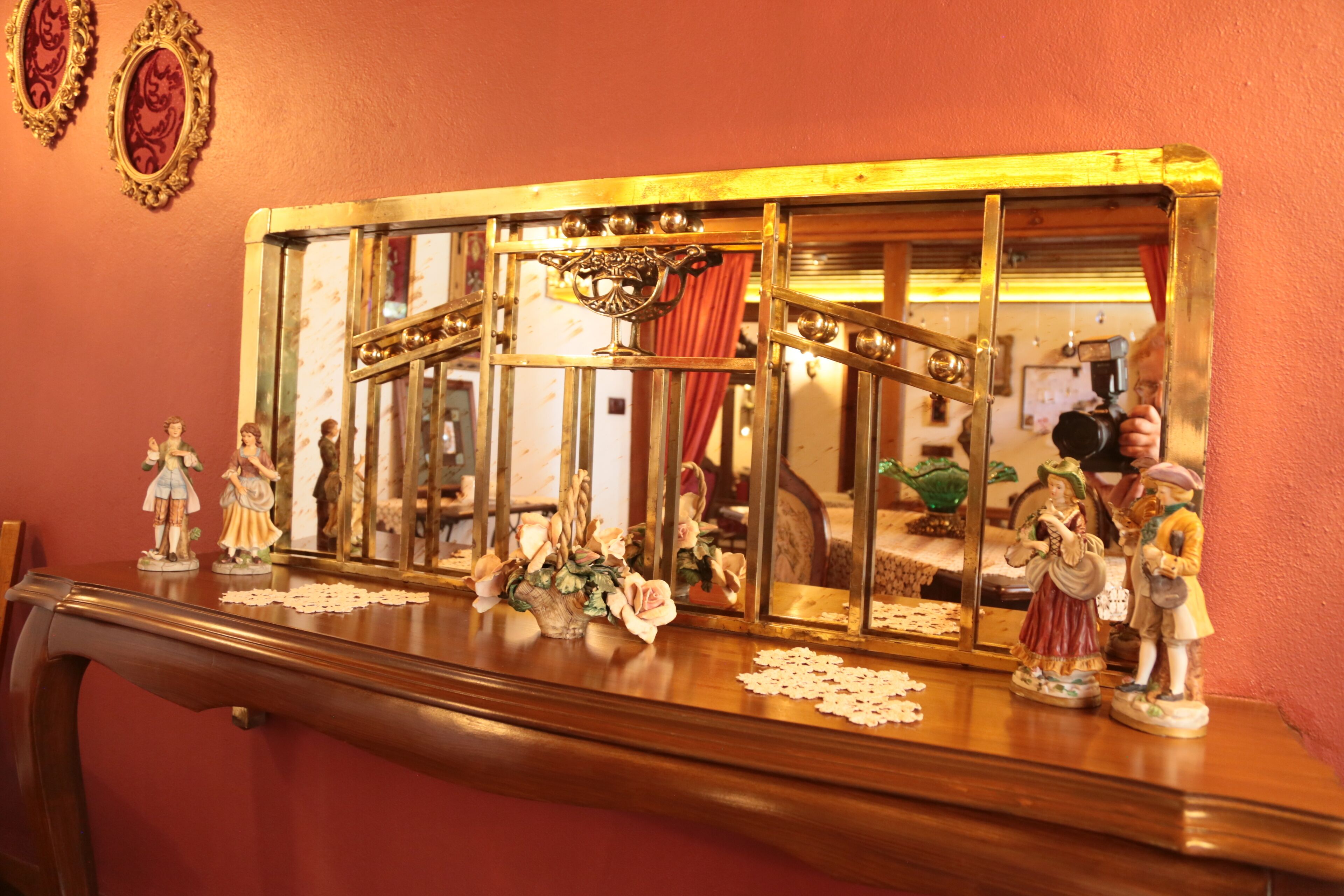 A wooden dresser with a mirror reflecting a room with a red curtain and a chandelier.