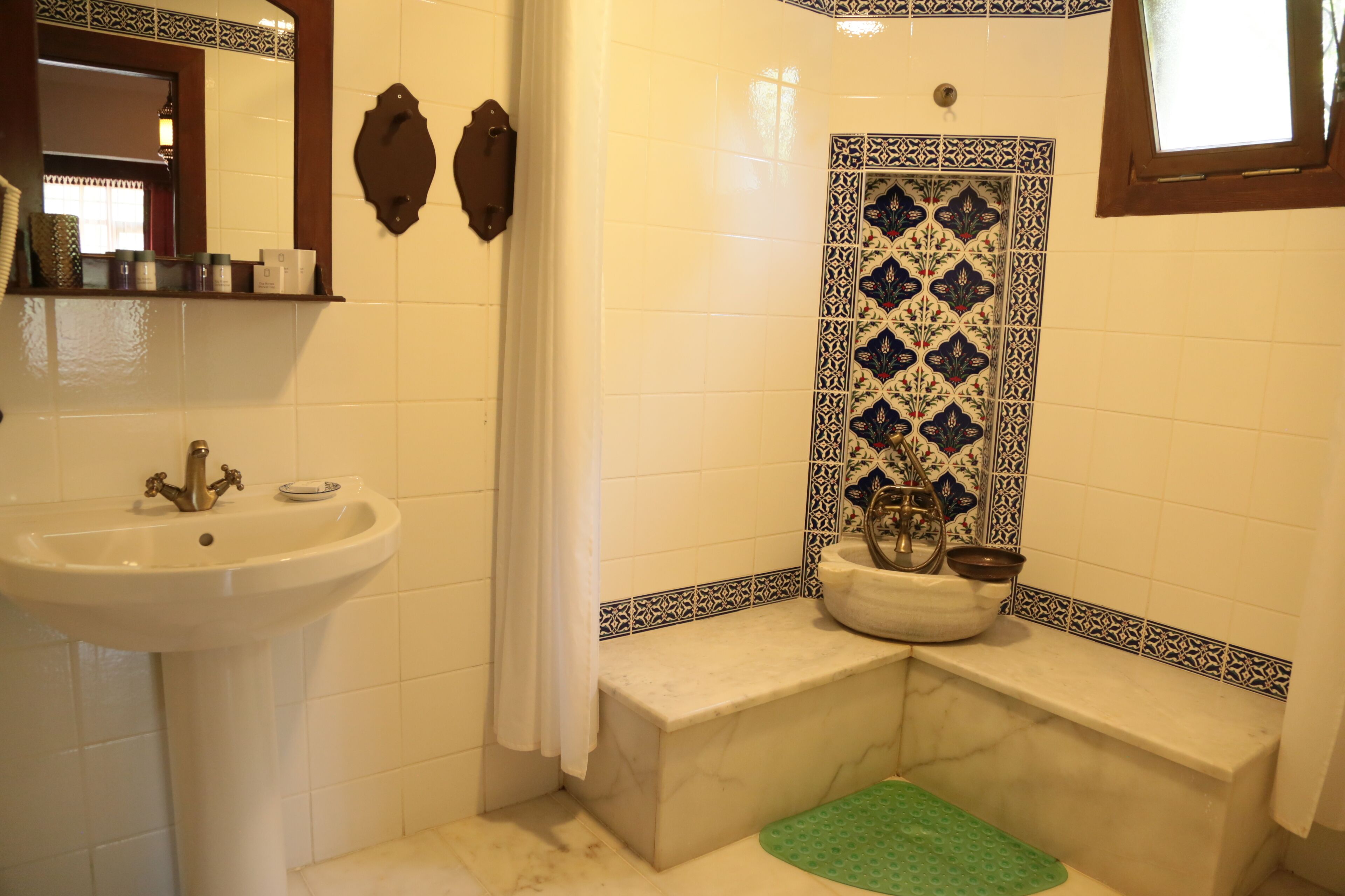 Un baño con lavamanos blanco, espejo, cortina de ducha, bañera y un revestimiento de azulejos decorativos.