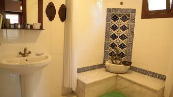 Un baño con lavamanos blanco, espejo, cortina de ducha, bañera y un revestimiento de azulejos decorativos.